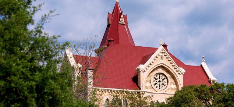 Main Building's steeple and roof from the side, framed by tree branches in the foreground.