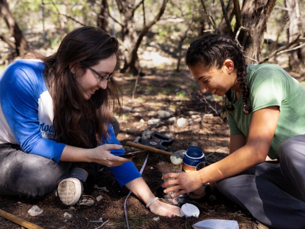 Two students sit on the ground and work on gathering data about the soil at Wild Basin.