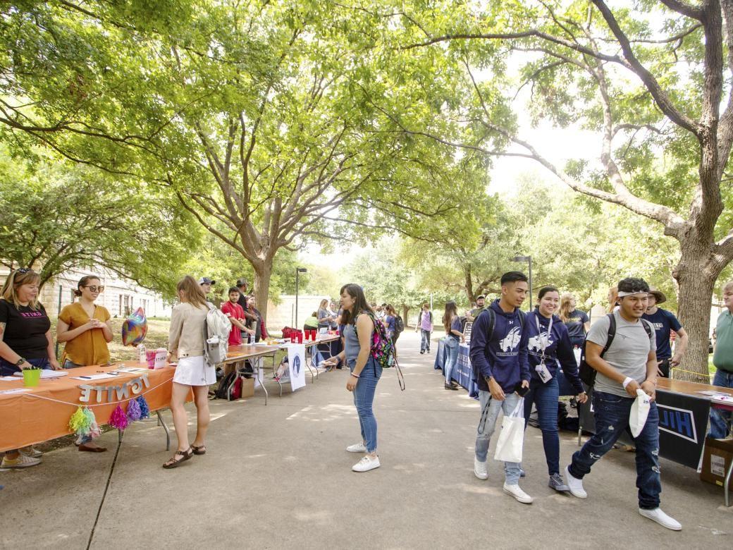 学生们走在一条头顶有树冠的小路上. 当学生停下来从其他学生那里获取信息时，路径上排列着表格, 教职员工.