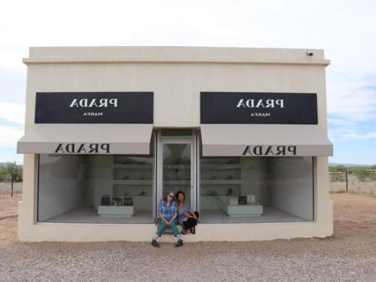 Two women sitting in front of a Prada store in the middle of the desert