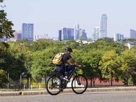 A student riding his bicycle on campus with downtown Austin in the background