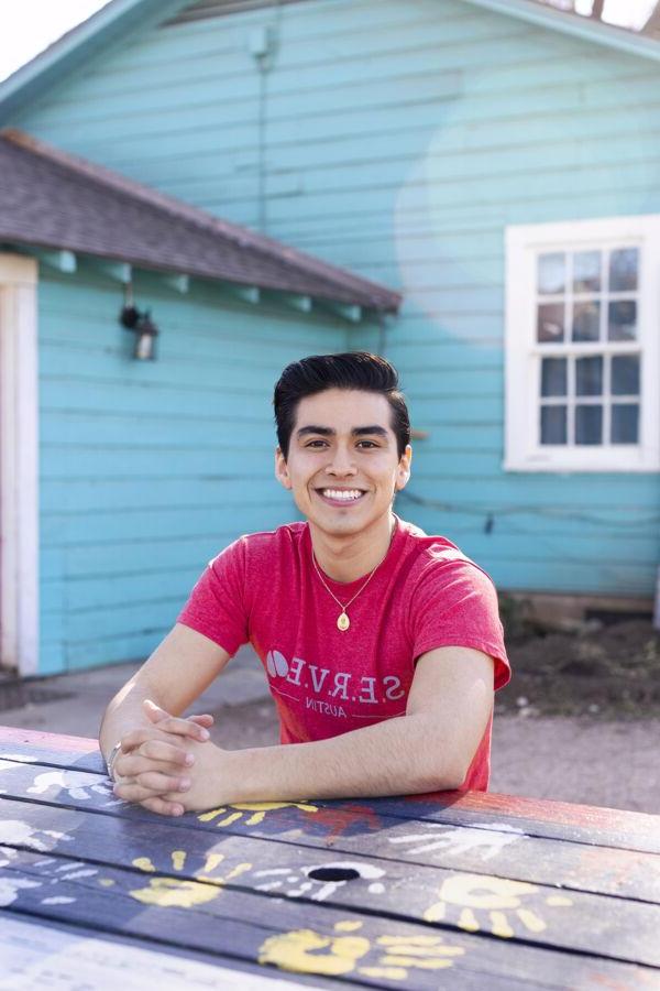 St. Edward's student Cristobal Diaz sits at a picnic table painted with colorful handprints.